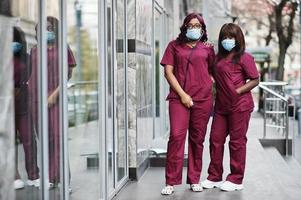 två afroamerikanska kvinnliga läkare på röd labbuniform i skyddande ansiktsmask. medicin, yrke och sjukvård koncept. stoppa coronavirusinfektion. foto