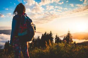 bakifrån vandrare backpacker på skogsstig njut av dramatisk solnedgång över moln i avlägsna Kaukasusberg varm sommarkväll foto