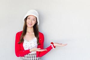 vacker asiatisk kvinna som bär röd kappa och vit hatt när en töntig tjej agerar med sin hand för att presentera något på den vita bakgrunden. foto
