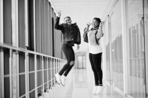 två afrikanska vänner i jeansjacka hoppar inomhus tillsammans. foto