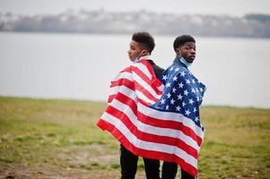 två afrikanska tonåringar vänner med amerikansk flagga i parken bär medicinska masker skyddar mot infektioner och sjukdomar coronavirus virus karantän. foto