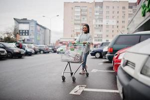 afrikansk kvinna med kundvagn vagn poserade utomhusmarknad nära parkering. foto