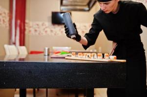 professionella kockkläder i svart gör sushi och rullar i ett restaurangkök med japansk traditionell mat. foto