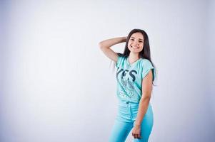 porträtt av en ung vacker kvinna i blå eller turkos t-shirt och byxor poserar i studion. foto