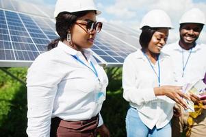 afrikansk amerikansk tekniker kontrollerar underhållet av solpanelerna. grupp om tre svarta ingenjörer som träffas på solstationen och gör en affär med pengar. foto