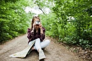 porträtt av en attraktiv blond tjej med en karta som sitter i skogen och tar bilder. foto