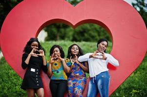 grupp av fyra afroamerikanska flickor mot stort rött hjärta utomhus. foto