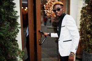 chic stilig afrikansk amerikansk man i vit kostym öppnade en dörr. foto