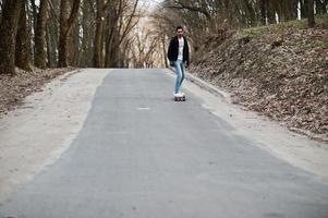 street style arabisk man i glasögon med longboard longboarding på vägen. foto