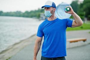 leverans vatten man bär skyddande ansikts medicinsk mask under coronavirus pandemi. foto