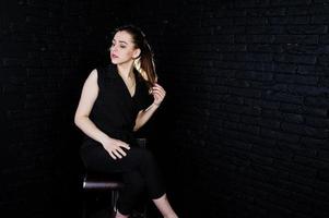 porträtt av en vacker brunett tjej i svart jumpsuit som sitter och poserar i studion. foto