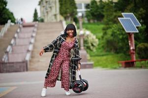 vacker afrikansk amerikansk kvinna håller i händerna segway eller hoverboard. svart flicka med dubbla hjul självbalanserande elektrisk skoter. foto