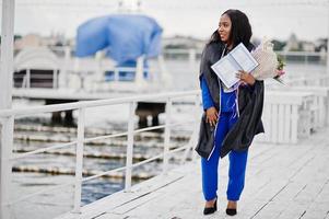 afrikansk amerikansk student flicka i svart examen klänning med diplom, på blå kostym poserade. foto