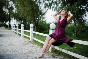 blond sensuell kvinna i röd marsala klänning poserar på stranden av resort. foto