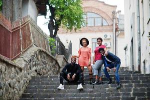 fyra afrikanska vänner som har roligt utomhus. två svarta tjejer med killar sitter på trappan i en gammal stad. foto