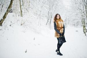 elegans lockig tjej i päls och handväska på snöig skogspark på vintern. foto