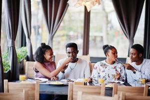 glada afrikanska vänner sitter, chattar på café och äter mat. grupp av svarta folk som träffas i restaurangen och äter middag. foto