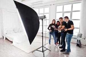 fotograf förklarar om skottet för sitt team i studion och tittar på en bärbar dator. prata med sina assistenter som håller i en kamera under en fotografering. lagarbete och brainstorm. foto