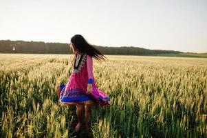 öm indisk flicka i saree, med violetta läppar utgör poserade på fältet i solnedgången. fashionabla indisk modell. foto