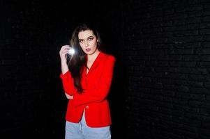 snygg brunett tjej på röd jacka mot studio svart tegelvägg. foto