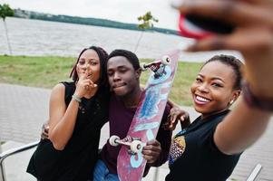 grupp av tre afroamerikanska vänner med skateboard gör selfie på telefonen. foto