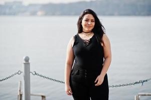 söt latino modell tjej från ecuador bär på svart poserade mot sjön. foto