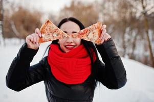 rolig brunett flicka utomhus på vintern med två bitar av pizza. foto