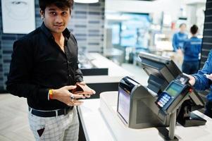 indisk man som håller plånbok bakom sin kassadisk med beställningsskärm och kortbetalningsterminal i matcafé. foto