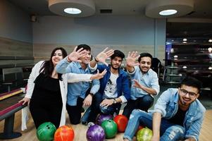 grupp av fem sydasiatiska folk som har vila och roligt på bowlingklubben. håller bowlingklot, sitter på gränden och ger high five med händerna. foto