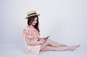 porträtt av en fashionabel kvinna i rosa klänning och hatt som sitter på golvet och tar selfie i studion. foto