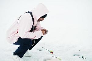 afrikansk amerikansk fiskare med fiskespö sitter på frusna havet. vinterfiske. foto