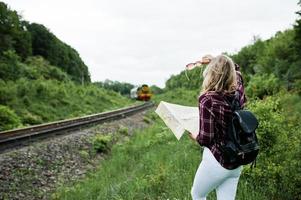 porträtt av en ung blondin i tartanskjorta bredvid tåget med en karta. foto