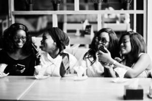 fyra afroamerikanska flickor som sitter på bordet på café med glassdessert och tittar på bilder på mobiltelefoner. foto
