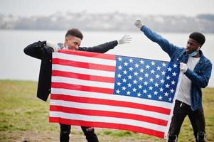 två afrikanska tonåringar vänner med amerikansk flagga i parken bär medicinska masker skyddar mot infektioner och sjukdomar coronavirus virus karantän. foto