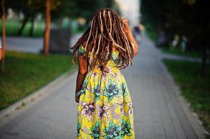 söt liten höjd afroamerikansk flicka med dreadlocks, bär på färgad gul klänning, poserade vid solnedgången. foto