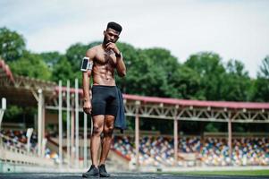 afrikansk amerikansk manlig idrottare sexig sport bar överkropp man med löpande sportarmfodral för mobiltelefon, poserade på stadion. foto