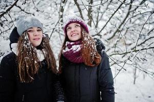 två roliga flickor vänner ha kul på vintern snöig dag nära snötäckta träd. foto