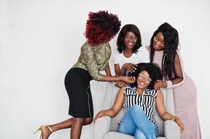glada ljusa positiva stunder av fyra afrikanska flickor. ha kul och ler på stol mot vit tom vägg. härliga stunder av fyra bästa vänner. foto