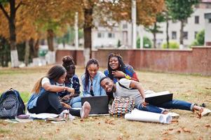 grupp på fem afrikanska högskolestudenter som spenderar tid tillsammans på campus på universitetsgården. svarta afro vänner sitter på gräs och studerar med bärbara datorer. foto