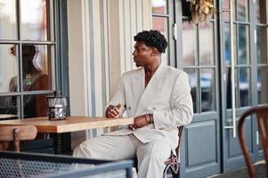 snygg afro man i beige old school kostym sitter på café. fashionabla ung afrikansk man i ledig jacka på bar överkropp. foto
