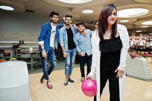 sydasiatisk kvinna står vid bowlinghall med boll på händerna. flickan förbereder sig för ett kast. vänner stöttar henne högt. foto