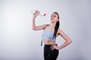 glada attraktiva unga fitness kvinna i topp och svarta leggings med hopprep och flaska vatten isolerad över vit bakgrund. foto