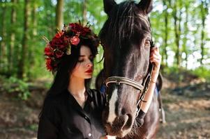 mystisk flicka i krans slitage i svart med häst i trä. foto