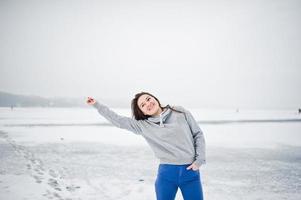 rolig tjej slitage på hoody tröja och jeans, vid frusen sjö i vinterdag. foto