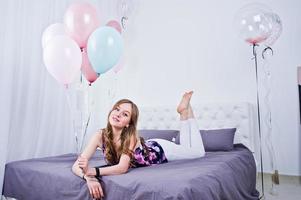 glad tjej med färgade ballonger på sängen på rummet. firande av födelsedagstema. foto
