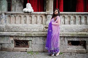 indisk hinduisk flicka på traditionell violett saree poserade på gatan mot gamla hus med röda gardiner. foto