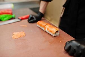 närbild händer av professionella kock bär i svarta handskar gör sushi och rullar i ett restaurang kök av japansk traditionell mat. foto