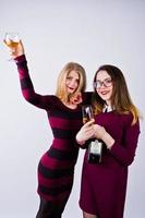 två attraktiva vänner i lila klänningar dricker mousserande vin eller champagne i studion. foto