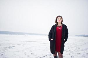 brunett plus size modell på rött mot frusen sjö på vinterdagen. foto