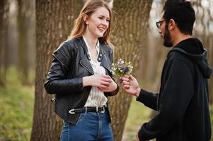 kärlekshistoria av coola mångrasiga par i vårskogen. man ger blommor till sin flickvän. foto